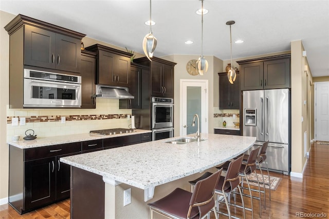 10057 Des Moines St, Parker, CO 80134 - kitchen with appliances with stainless steel finishes, a sink, under cabinet range hood, wood finished floors, and a center island with sink