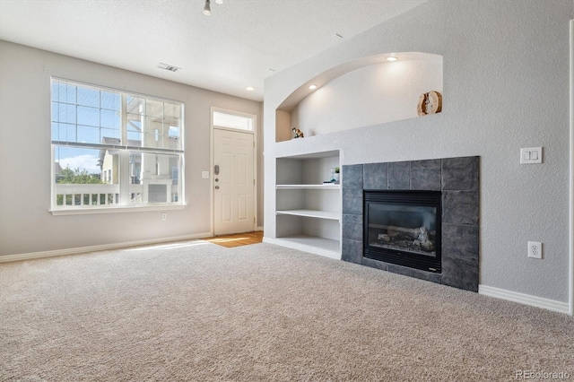 unfurnished living room featuring carpet, built in features, baseboards, a fireplace, and a textured wall