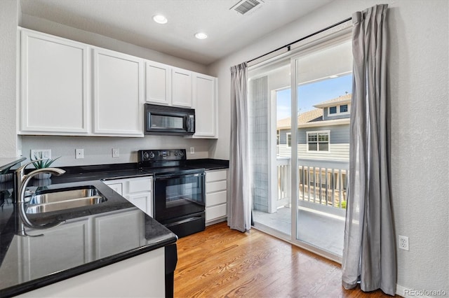 kitchen with black appliances, a sink, white cabinetry, dark countertops, and light wood-style floors