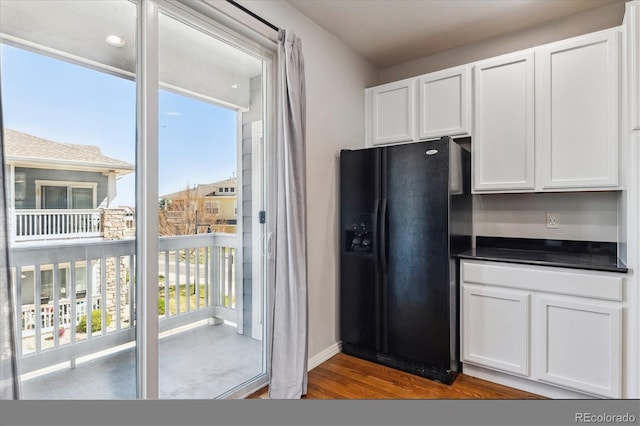 kitchen with black refrigerator with ice dispenser, dark countertops, white cabinetry, and wood finished floors