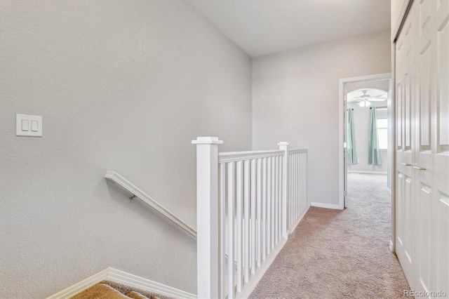 corridor with an upstairs landing, carpet floors, and baseboards