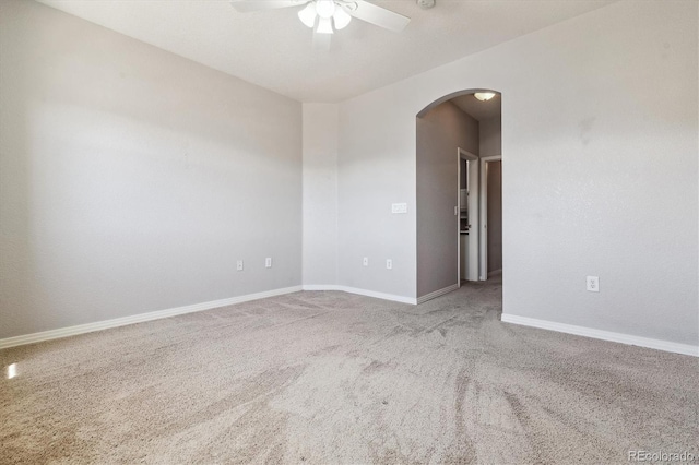 carpeted empty room with arched walkways, ceiling fan, and baseboards