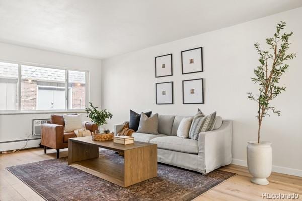 living area with baseboards, a wall unit AC, baseboard heating, and wood finished floors