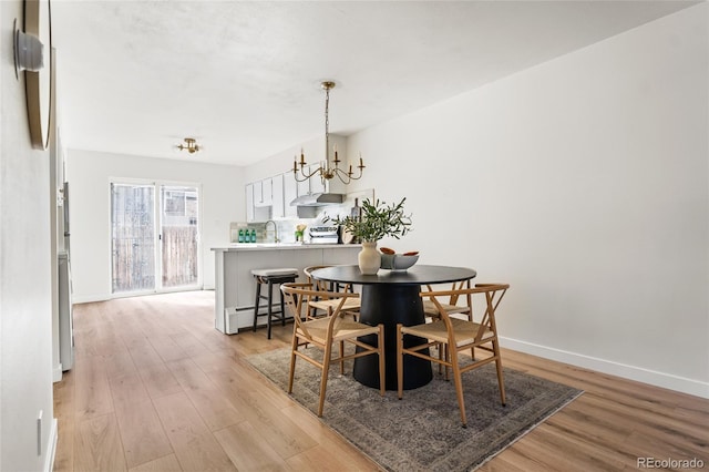 dining space featuring light wood finished floors, a baseboard radiator, baseboards, and a notable chandelier