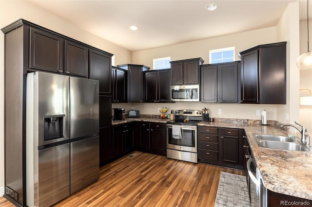 kitchen with stainless steel appliances, dark hardwood / wood-style floors, decorative light fixtures, dark stone countertops, and sink