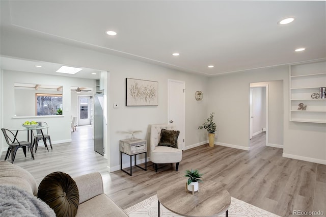 living room featuring baseboards, light wood-type flooring, a skylight, and recessed lighting