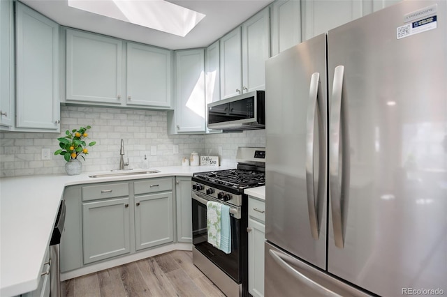 kitchen with stainless steel appliances, tasteful backsplash, light countertops, a sink, and light wood-type flooring