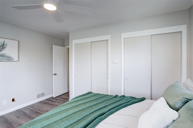 bedroom featuring visible vents, baseboards, a ceiling fan, wood finished floors, and multiple closets