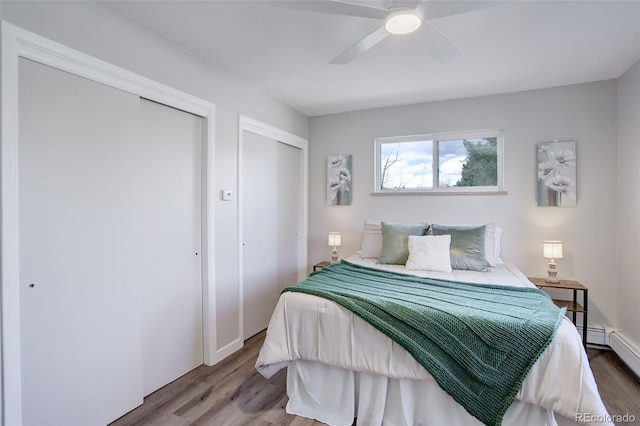 bedroom featuring two closets, a ceiling fan, a baseboard heating unit, and wood finished floors