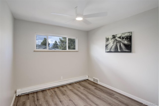 empty room featuring a baseboard heating unit, wood finished floors, visible vents, and baseboards