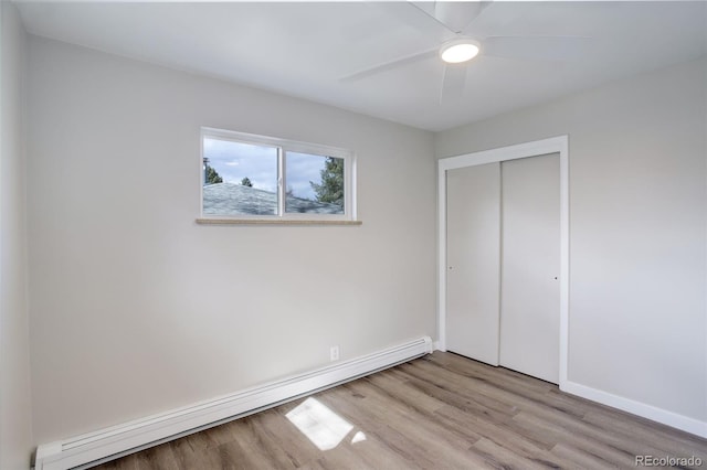 unfurnished bedroom with a closet, baseboard heating, ceiling fan, wood finished floors, and baseboards