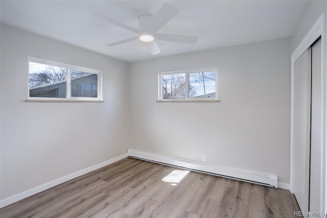 unfurnished bedroom with a baseboard radiator, baseboards, a closet, and wood finished floors