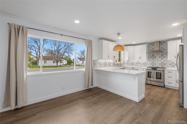 kitchen with stainless steel appliances, wood finished floors, wall chimney range hood, a sink, and a peninsula