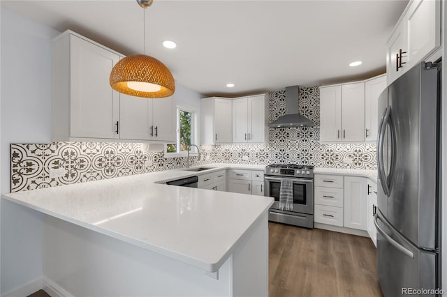 kitchen with stainless steel appliances, light countertops, wall chimney range hood, a sink, and a peninsula