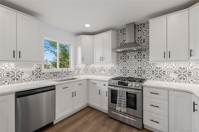 kitchen with stainless steel appliances, a sink, white cabinetry, wall chimney range hood, and light countertops