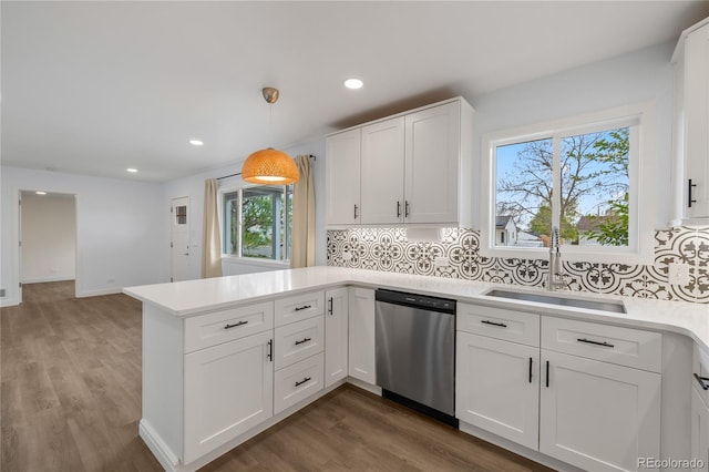 kitchen featuring a peninsula, stainless steel dishwasher, a sink, and light countertops