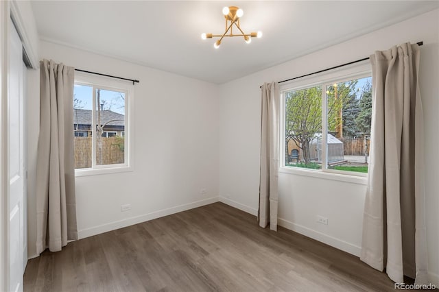 unfurnished room with wood finished floors, baseboards, and an inviting chandelier