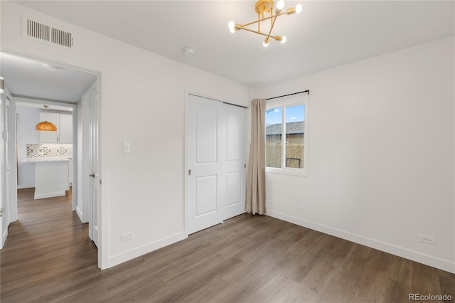 unfurnished bedroom featuring an inviting chandelier, wood finished floors, visible vents, and baseboards