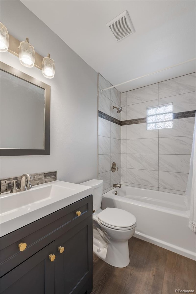 bathroom featuring wood finished floors, vanity, shower / bath combination, toilet, and visible vents