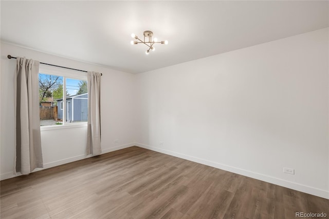 unfurnished room featuring baseboards, wood finished floors, and a chandelier