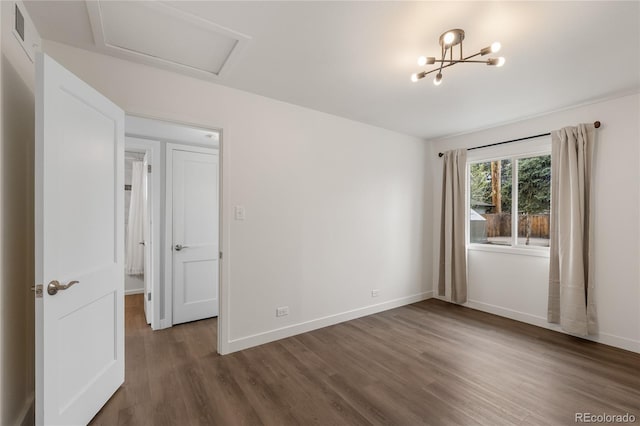 unfurnished room featuring attic access, baseboards, an inviting chandelier, visible vents, and wood finished floors