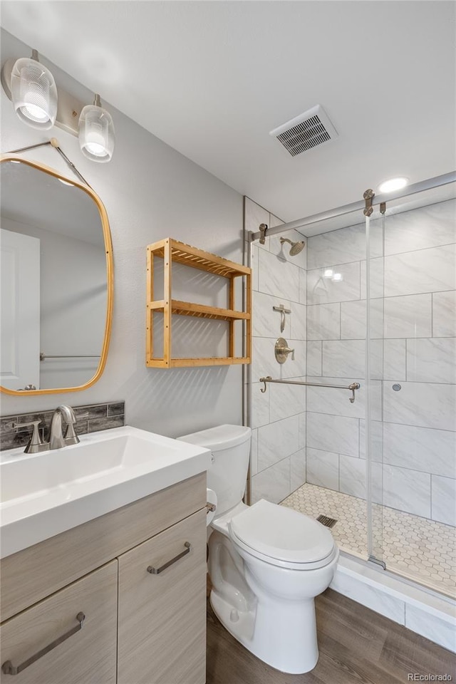 bathroom with toilet, visible vents, wood finished floors, a shower stall, and vanity