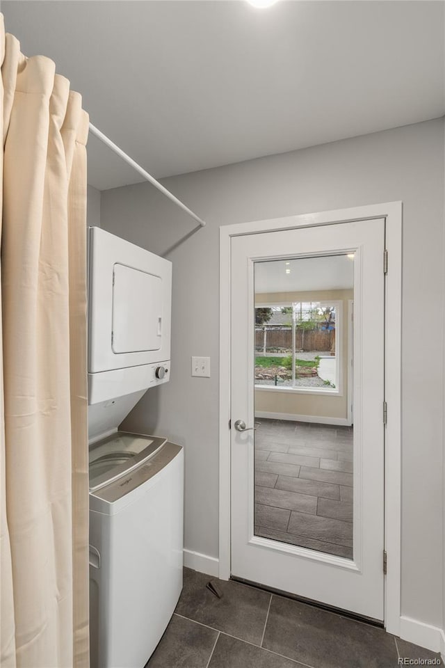 laundry room featuring baseboards, stacked washer and clothes dryer, dark tile patterned floors, and laundry area