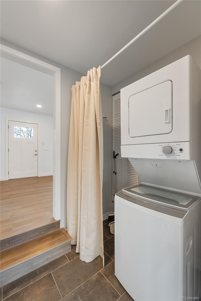 clothes washing area with stacked washer / drying machine, baseboards, tile patterned flooring, and laundry area
