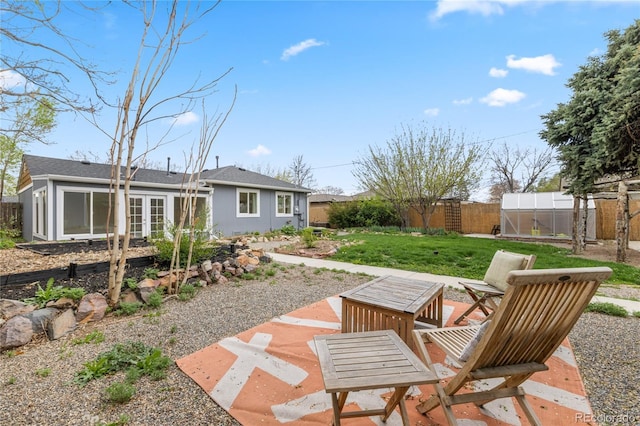 view of yard with a fenced backyard, a patio area, a greenhouse, and french doors