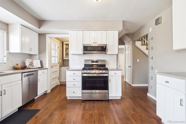 kitchen featuring backsplash, dark wood-style flooring, appliances with stainless steel finishes, baseboards, and white cabinetry