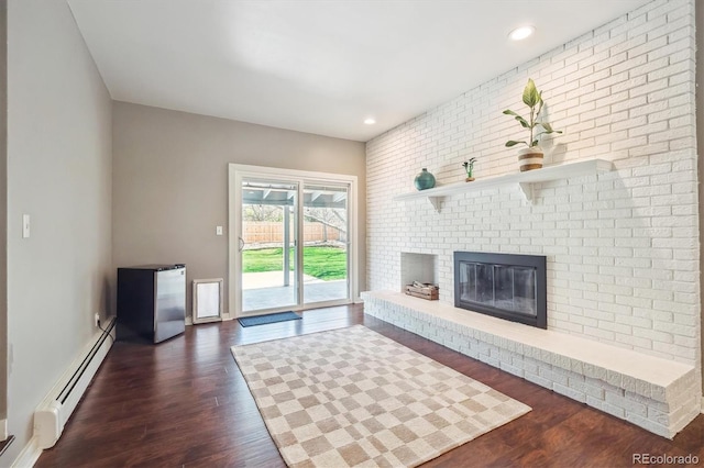 unfurnished living room with dark wood-style flooring, a baseboard heating unit, recessed lighting, and a fireplace