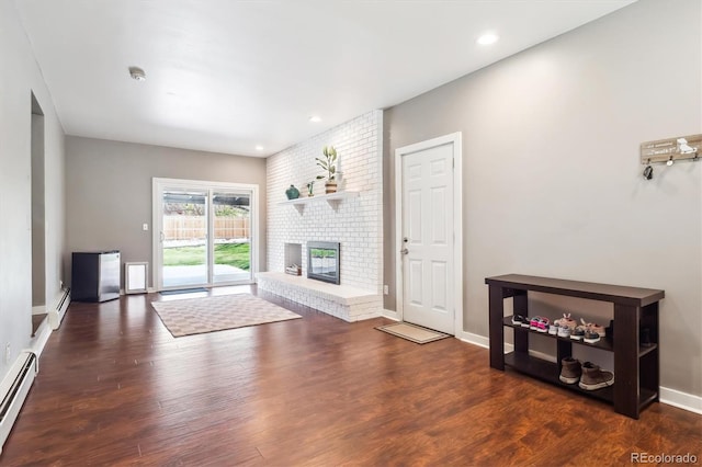 unfurnished living room with a fireplace, a baseboard heating unit, and wood finished floors