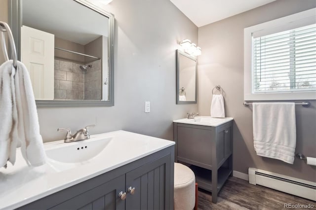 bathroom featuring a sink, wood finished floors, baseboard heating, and two vanities