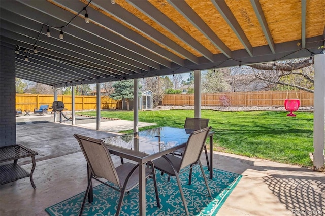 view of patio / terrace with a fenced backyard, a storage unit, outdoor dining space, and an outdoor structure