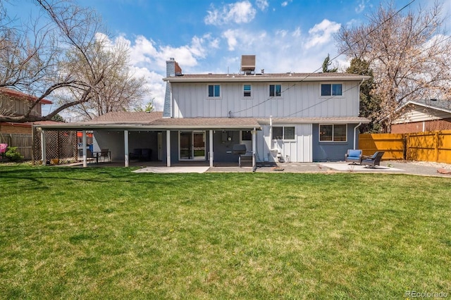 back of house with fence, board and batten siding, a chimney, a lawn, and a patio