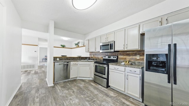 kitchen with a textured ceiling, stainless steel appliances, dark stone counters, decorative backsplash, and light hardwood / wood-style floors