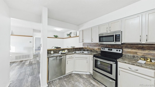 kitchen with backsplash, light hardwood / wood-style floors, sink, white cabinetry, and stainless steel appliances