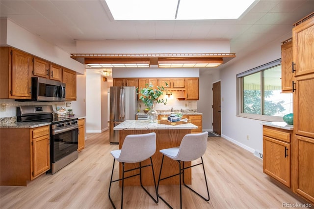 kitchen featuring light wood-style flooring, stainless steel appliances, a breakfast bar, baseboards, and a center island