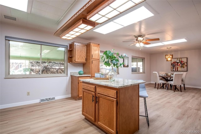 kitchen with a skylight, baseboards, light wood-style flooring, a kitchen island, and a kitchen bar