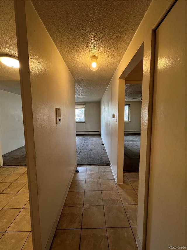 hall with tile patterned floors, baseboard heating, and a textured ceiling