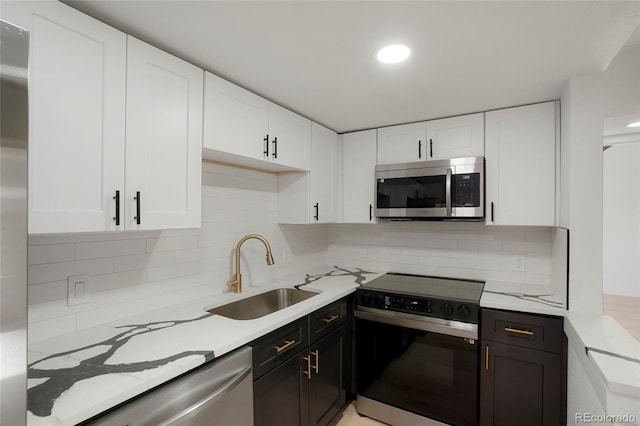 kitchen featuring decorative backsplash, light stone counters, stainless steel appliances, sink, and white cabinets