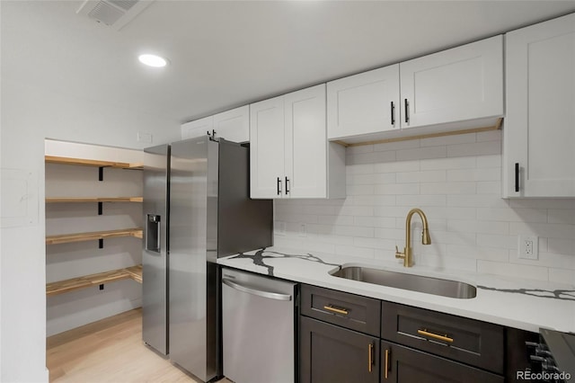 kitchen with backsplash, light stone counters, stainless steel appliances, sink, and white cabinets