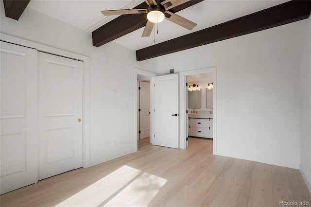 unfurnished bedroom featuring ceiling fan, light hardwood / wood-style flooring, beamed ceiling, ensuite bathroom, and a closet