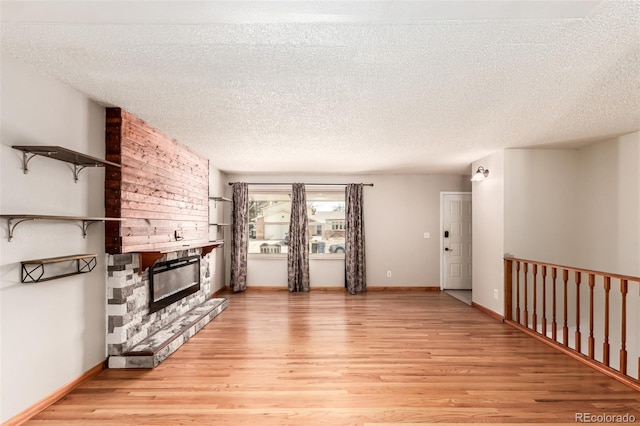 unfurnished living room with light wood finished floors, a stone fireplace, a textured ceiling, and baseboards