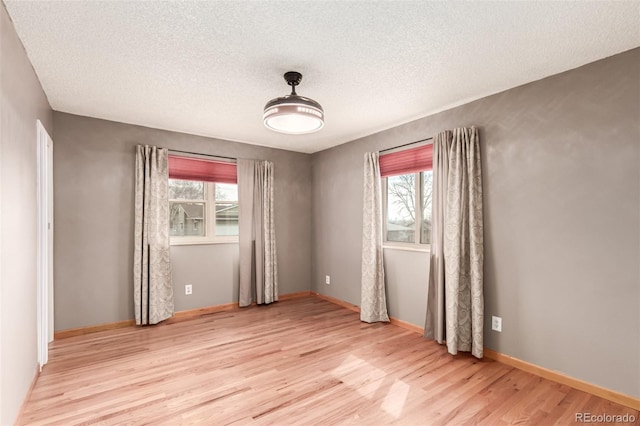 spare room with light wood-style floors, baseboards, and a textured ceiling