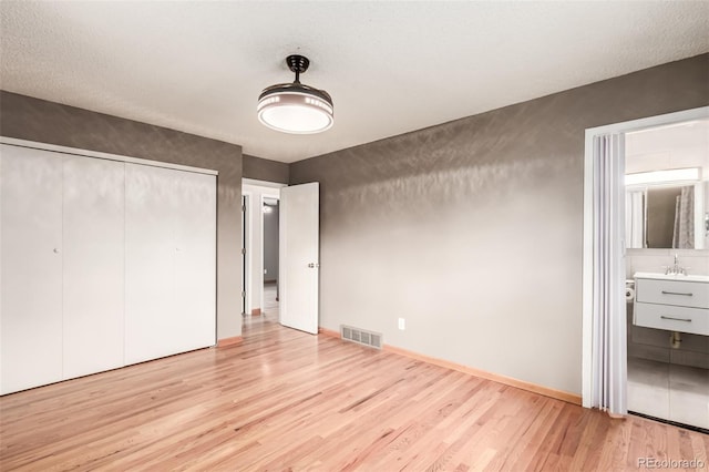 unfurnished bedroom with a sink, visible vents, baseboards, light wood finished floors, and ensuite bath