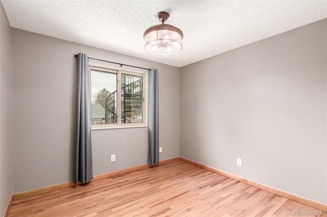 unfurnished room featuring baseboards, light wood-style flooring, and a textured ceiling