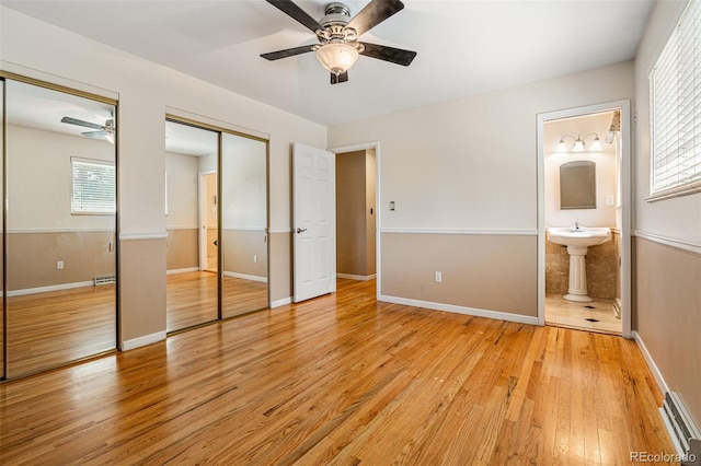 unfurnished bedroom featuring ceiling fan, connected bathroom, light wood-type flooring, and two closets