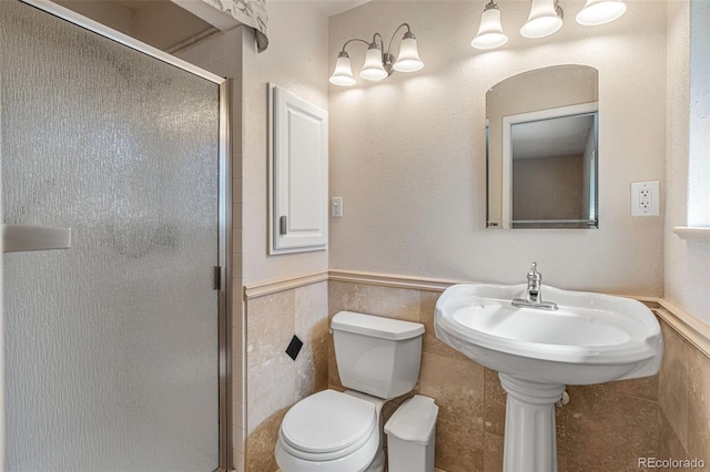 bathroom featuring a shower with shower door, tile walls, and toilet