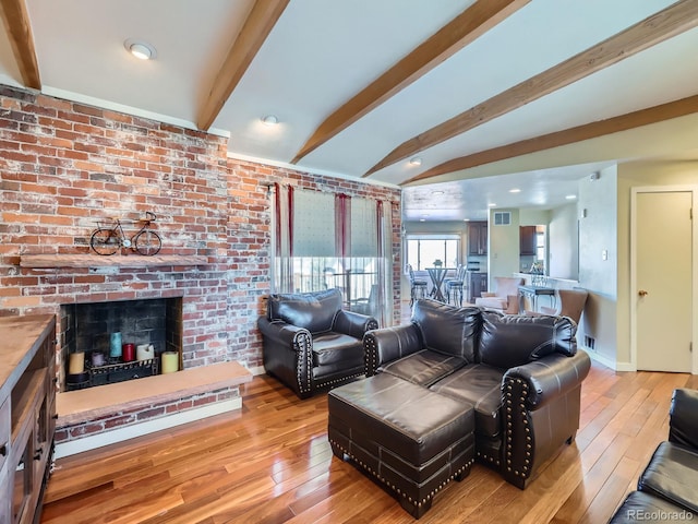 living room featuring beam ceiling, a fireplace, brick wall, and light hardwood / wood-style flooring